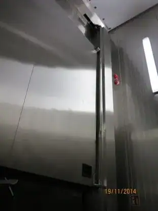 Vista frontal de una puerta guillotina de acero inoxidable instalada en planta de producción alimentaria.