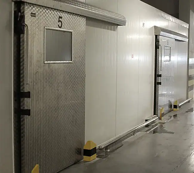 Puerta vía de carriles con ventana de cristal y marco antiácido en cámara frigorífica industrial.