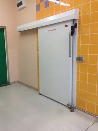 Wieja, puertas industriales, imagen de una puerta para cámara de refrigeración empotrada a una pared amarilla. 