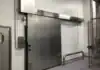 Puerta automática corrediza de una hoja fabricada en acero inoxidable, ideal para entornos industriales que requieren higiene y control térmico.