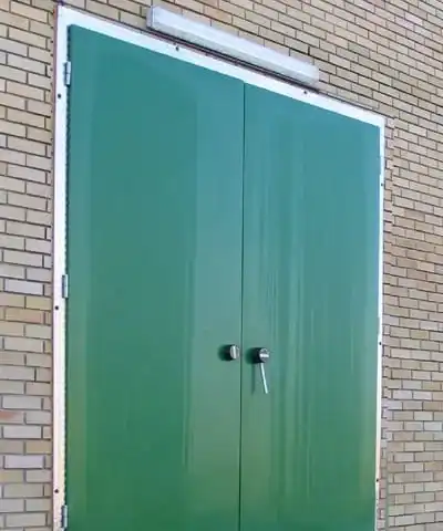 Puerta cámara frigorífica de doble hoja verde con bisagras para entrada exterior en área de carga.