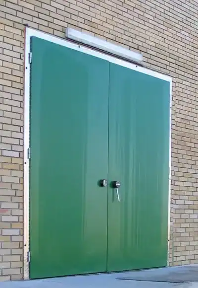 Puerta cámara frigorífica de doble hoja verde con bisagras para entrada exterior en área de carga.